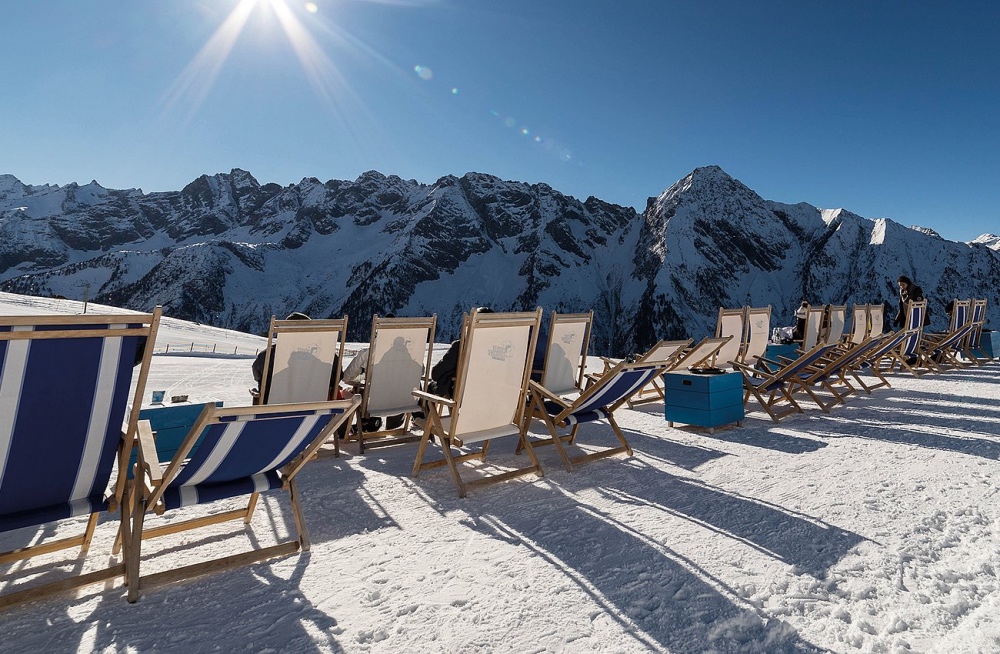 Liegestühle auf Schnee mit Sonne und Blick auf die Berge